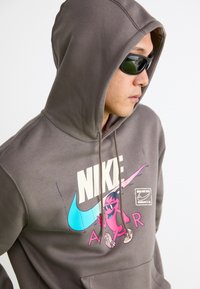 Grå hættetrøje med grafisk tryk af en livlig karakter og Nike-logoet, med justerbar hætte og frontlomme.