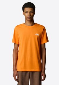 Orange bomulds T-shirt med korte ærmer og rund hals. Har et hvidt logo på venstre bryst. Glat tekstur og normal pasform.
