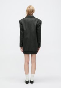 Sacou oversized de culoare gri închis, cu umeri ascuțiți, asociat cu o fustă mini coordonată. Prezintă țesătură texturată și manșete cu nasturi.