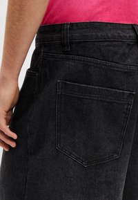 Schwarze Denim-Hose mit entspanntem Schnitt, ausgestattet mit einer Gesäßtasche, sichtbaren Nahtdetails und einer glatten Textur.