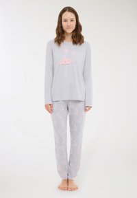 Giovane donna in piedi a piedi nudi, indossa un pigiama grigio con stampe a tema balletto rosa e una grafica di ballerina sulla parte superiore.