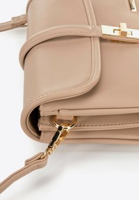 Borsa a tracolla in pelle beige con angolo e chiusura dorata, dotata di gancio per cinturino rimovibile, su sfondo bianco.