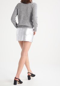 Stříbrná džínsová mini sukně s třepeným lemem, kombinovaná se šedým svetrem s dlouhým rukávem a černými sandály na blokovém podpatku.