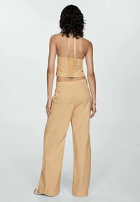 Top corto halter de un beige claro con tirantes finos, combinado con pantalones holgados de pierna ancha que cuentan con bolsillos traseros y una textura suave.