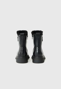 Zwarte leren enkellaarzen met een textuur van nepbont rond de kraag en zijritsen. Voorzien van een robuuste rubberen zool voor extra grip en ondersteuning.