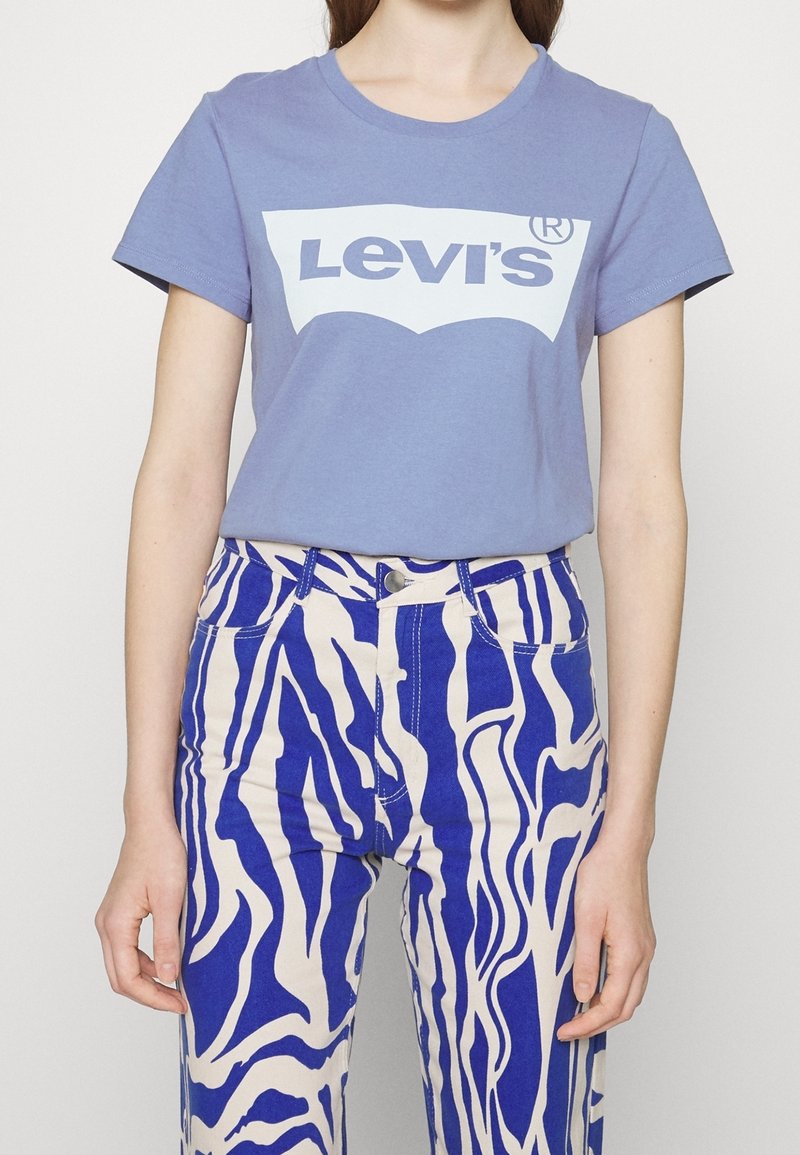 Personne portant un t-shirt violet Levi's et un pantalon taille haute avec un imprimé zèbre abstrait bleu et blanc.