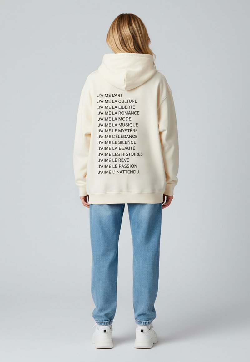 Felpa crema con testo nero che elenca vari interessi, abbinata a pantaloni della tuta azzurri chiari e sneakers bianche. Materiale morbido, vestibilità rilassata.