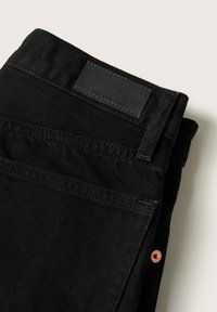 Jeans de mezclilla negra doblados cuidadosamente, con una etiqueta de cuero, acentos de remaches de cobre y una textura suave. Costuras visibles a lo largo de los bordes.