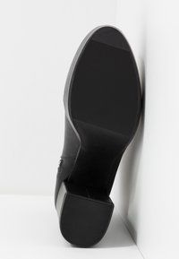 Bota de cuero negro con tacón cuadrado y suela de goma texturizada. El tacón es resistente y la bota presenta un detalle de costura mínimo.