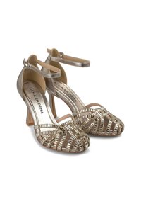 Scarpe con tacco alto dorate con design open-toe, caratterizzate da accenti metallici e una fascia decorata con fibbia, montate su un tacco a blocco trasparente.