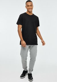 Camiseta de algodón negra de manga corta, combinada con pantalones de chándal grises. Zapatillas negras con suelas blancas. Textura suave, diseño casual.