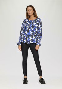 Vloeiende blouse in blauw en zwart met een patroon en lange mouwen, gecombineerd met glanzende zwarte leggings en zwarte instappers. Soepele stof, ronde halslijn.