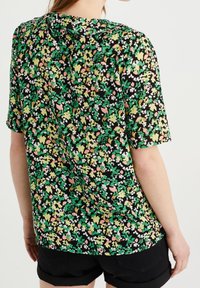 Short-sleeve blouse featuring a black base with a colorful floral pattern in green, pink, and white. Soft fabric with a relaxed fit.