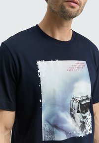 Tricou bleumarin cu mânecă scurtă, realizat din bumbac. Prezintă o imprimare grafică mare a unui vehicul în zăpadă, cu accente albe în jurul designului.
