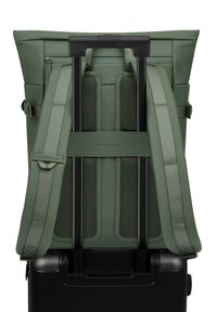 Groene rugzak ontworpen voor reizen, voorzien van gaasvering, verstelbare schouderbanden en kan bevestigd worden aan een zwarte koffer met wielen.