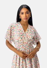 Blumenkleid aus leichtem Stoff mit V-Ausschnitt und kurzen, flatternden Ärmeln. Verfügt über eine geraffte Taille und ein buntes Blumenmuster auf der gesamten Fläche.
