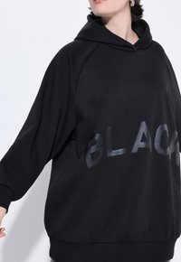 Zwarte hoodie van zachte stof met een relaxte fit. Voorzien van grote, glanzende "BLACK" opdruk aan de voorkant en geribde manchetten en onderkant.