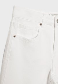 Jean en denim blanc montrant la partie supérieure avant avec une poche, des rivets métalliques, des passants de ceinture et une étiquette de taille partiellement visible.
