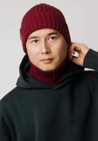 Bordowa prążkowana dzianinowa czapka z dopasowaną kominow�ą apaszką, wykonana z miękkiego materiału. Noszona z czarną bluzą z kapturem, podkreślając teksturowane detale.