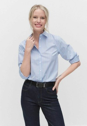 Light blue button-up shirt with white and pink vertical stripes, featuring a collar and rolled-up sleeves, paired with dark denim jeans and a black belt.