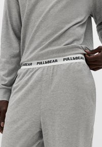 Szary bawełniany komplet do noszenia w domu z długimi rękawami i elastycznym pasem w talii z czarnym logo "PULL&BEAR". Zbliżenie na szczegóły pasa.