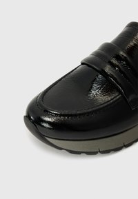 Black patent leather loafer with rounded toe, textured surface, and two decorative straps across the front. Grey outsole with tread pattern.