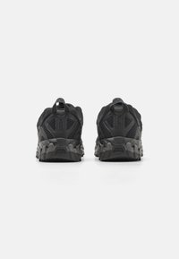 Black athletic shoes with a mesh upper and reinforced heel. They feature a textured, lugged sole for traction and a pull tab at the back.