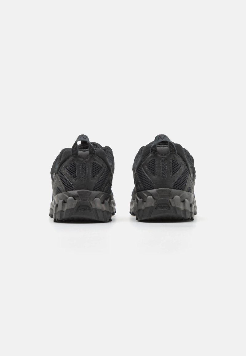 Schwarze Sportschuhe mit einem Obermaterial aus Mesh und verstärktem Fersenbereich. Sie verfügen über eine strukturierte, profilierte Sohle für Traktion und eine Zuglasche an der Rückseite.