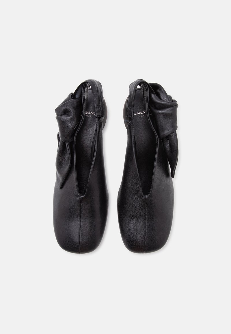 Paar schwarze flache Lederschuhe mit offenem Fersenbereich und gedrehtem Schleifendetail an den Knöchelriemen, von oben auf weißem Hintergrund gezeigt.