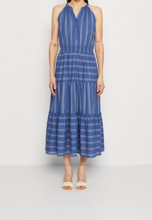 Robe midi bleue sans manches avec des rayures blanches verticales et horizontales, encolure boutonnée, taille élastique, portée avec des sandales blanches tressées à bout ouvert.
