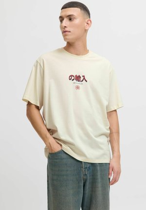 Beige oversize tričko s grafickým textem v tmavě červené barvě, vyrobené z jemné bavlny, s krátkými rukávy, spárované s volnými světlomodrými džíny.