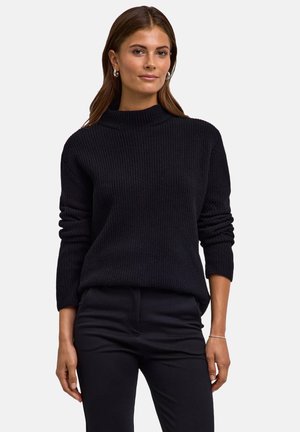 Maglione nero a coste con colletto alto e maniche lunghe, caratterizzato da una vestibilità comoda e una superficie tessile. Abbinato a pantaloni neri.