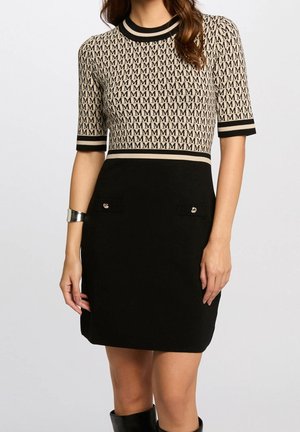 Vestido hasta la rodilla con parte superior beige cubierta con patrón repetitivo de "M", falda negra con bolsillos delanteros, mangas cortas y cuello y puños a rayas.