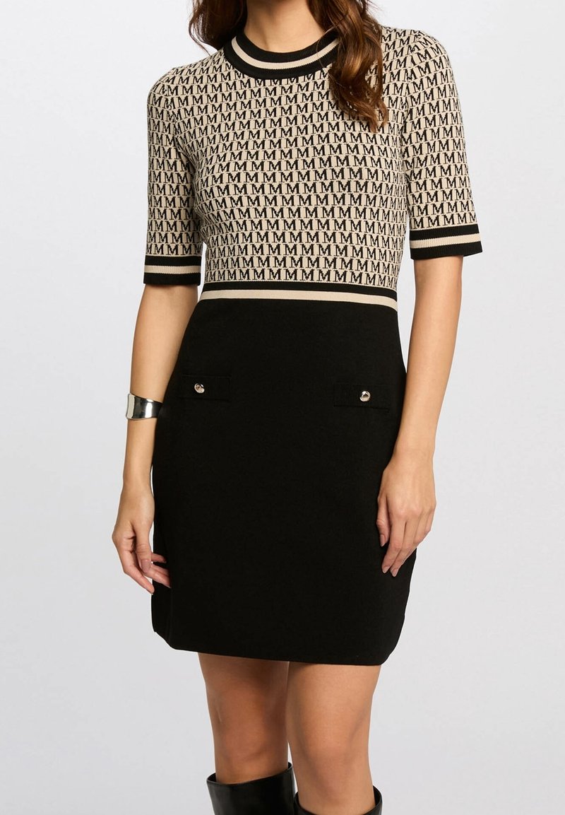 Robe longueur genou avec haut beige recouvert d’un motif répétitif « M », jupe noire avec poches avant, manches courtes, et col et poignets rayés.