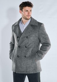 Grau melierter Wollmischmantel mit doppelreihiger Knopfleiste, großen schwarzen Knöpfen, Seitentaschen und breitem Kragen, getragen über einem gestreiften Hemd.