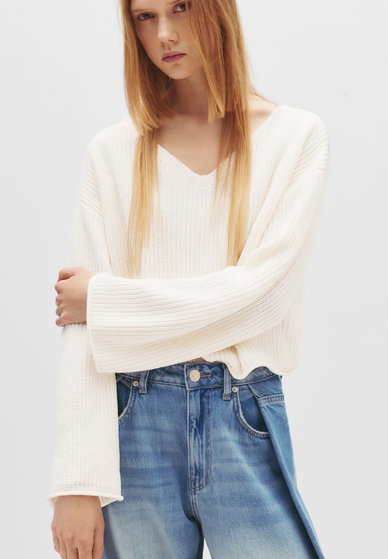 Maglione a coste color crema con scollatura a V e maniche oversize, abbinato a jeans in denim blu chiaro con vestibilità comoda e orlo sfrangiato.