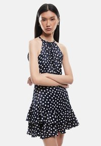 Vestido de halter náutico con lunares blancos, que presenta un dobladillo con volantes y una tela ligera. El diseño incluye un escote recogido y una silueta ajustada.