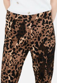 Nohavice s leopardím vzorom v hnedej a čiernej farbe, so širokým pásom a hladkým povrchom, s priliehavým strihom.