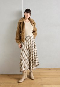 Brun fuzzy jakke, beige tætsiddende top og en plaid midi-nederdel med creme, brun og grønne nuancer. Beige hælede ankelstøvler.