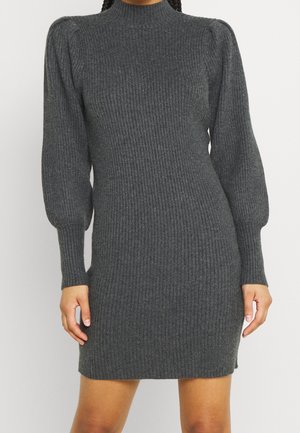 Woman wearing a dark gray ribbed knit sweater dress with long puffed sleeves and a mock neck, standing against a plain light background.