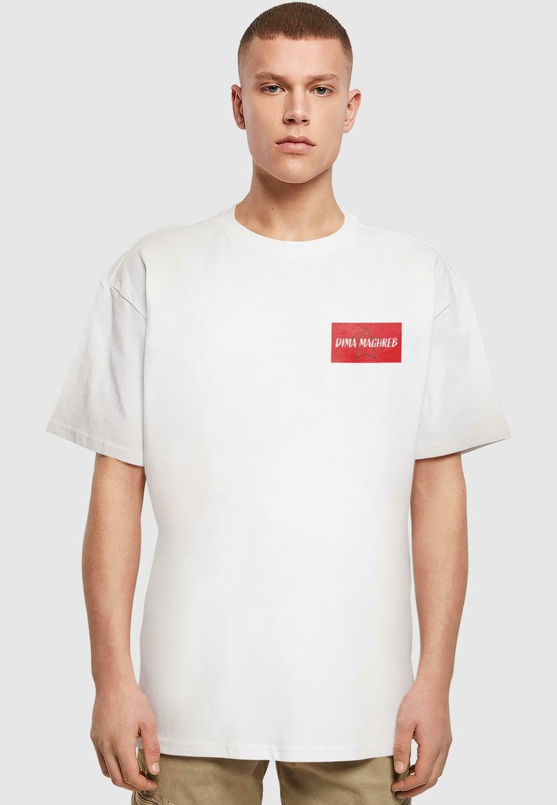 White cotton T-shirt with short sleeves, featuring a red rectangular patch with "DIMA MAGHREB" text and a star design. Relaxed fit.