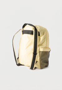 Ανοιχτόκίτρινο σακίδιο πλάτης με μαύρους ρυθμιζόμενους ιμάντες ώμου και πλαϊνή τσέπη από δίχτυ, σε απλό λευκό φόντο.