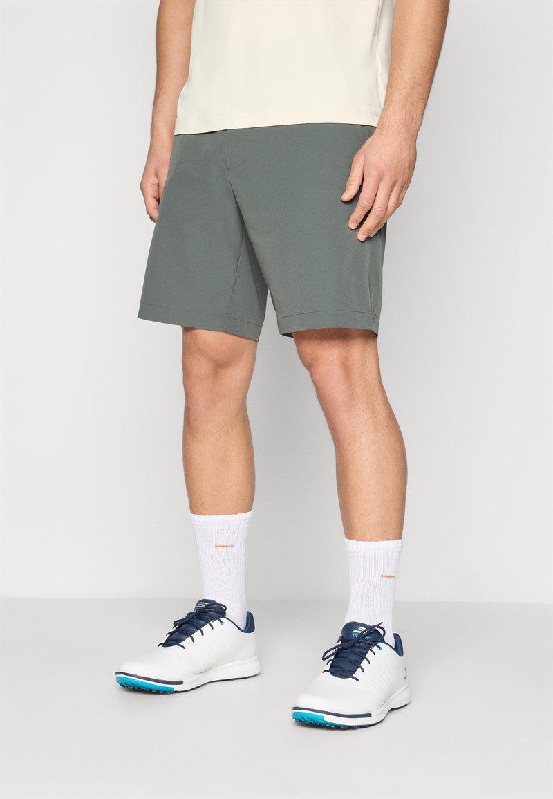 Ανδρικές γκρίζες βερμούδες φτιαγμένες από ελαφρύ ύφασμα, με ίσια γραμμή και τσέπες. Συνδυασμένες με λευκά αθλητικά παπούτσια και λευκές ριμπ κάλτσες.