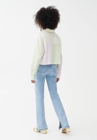 Camicia tagliata, a blocchi di colore in verde chiaro e rosa, con maniche lunghe. Abbinata a jeans flare azzurri e sandali con tacco quadrato beige.