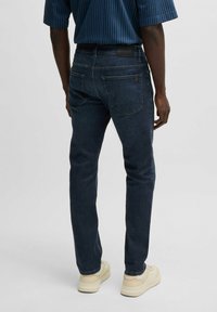 Mörkblå denimjeans med slim fit, som har två bakfickor och en läderpatch vid midjan. Slät textur och rak bendesign.