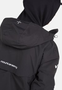 Veste noire imperméable avec capuche, dotée d'un col haut, de poignets ajustables et de détails de marque blancs. Texture lisse et design léger.
