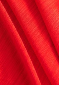 Tissu rouge avec une texture lisse et des lignes subtiles, plié de manière à mettre en valeur sa couleur vibrante et son apparence légère.