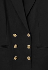 Blazer nero con design a doppio petto, sei bottoni dorati, dettagli ricamati neri e due tasche laterali. Tessuto morbido.