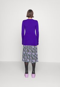 Lila långärmad topp med ribbat mönster, kombinerad med en blommönstrad kjol i dämpade gröna och lila nyanser. Svarta strumpbyxor och rosa platåskor.