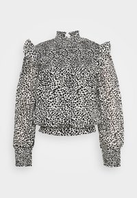 Svart och vit prickig blus med hög hals, smockad kropp och långa ärmar med elastiska manschetter och volangdetaljer på axlarna.